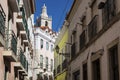 View of a narrow street and buildings with a tower of the Sao Vincente de Fora church on the backrgound, in the historic neighbour