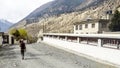 Nepali man walking past a mani wall with Tibetan Buddhism prayer wheels in Marpha village Annapurna Circuit Nepal