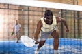 View through net of african american playing paddle on indoor court
