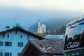 View of the Neuschwanstein castle over the roofs of houses in the fog in the morning