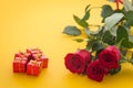 Occasional beautiful red roses with boxes of gifts on the yellow background with place for dedications or wishes