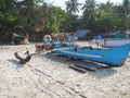 A view of an old battered blue wooden fishing boat standing on a sandy beach