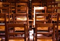 View on old brown wood chairs with backrest in a row inside catholic empty church illuminated by natural sun light