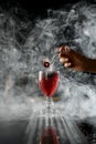 View on old fashioned cocktail glass with red liquid and woman& x27;s hand holding small fork with Pastille above it Royalty Free Stock Photo