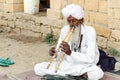 Old Indian man in traditional white clothing playing double flutes in Jaisalmer desert Rajasthan India