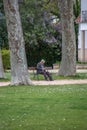 View of old man sitting on a bench, behind the garden trees, resting and looking around the park.olderTomar / Portugal - 04 04 Royalty Free Stock Photo