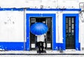 View on Old man with umbrella in front of blue colored building in the city of Ericeira, Portugal Royalty Free Stock Photo