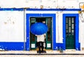 View on Old man with umbrella in front of blue colored building in the city of Ericeira, Portugal Royalty Free Stock Photo