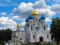 View of old Orthodox white stone church with gold and blue domes in monastery against background of green trees and cloudy sky. Royalty Free Stock Photo
