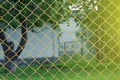 View through the old rusty yellow iron bars mesh netting on the fence. Green tree and grass in the background Royalty Free Stock Photo