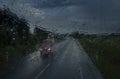 view of the oncoming car on the highway with the headlights turned on through glass wet from heavy rain in drips and drops in very