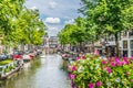 View of one of the canals in Amsterdam. Very flowery bridge and many tourists in the streets on a summer afternoon