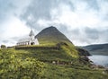 View onto the church of Vidareidi also named Vidareidi Kirkja with moody cloudy sky, fog and mountains. Faroe Islands