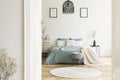 A view through an open door into a sunny bedroom interior with sage color linen and cushions on a bed, blanket, drawer cabinet, so Royalty Free Stock Photo