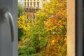 View from the open window of the apartment on autumn trees with colorful bright foliage and an old building on a city street. Royalty Free Stock Photo