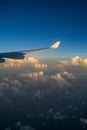 View out of airplane window with clouds at sunset and airplane wing.