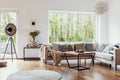 View outside to the green woods through large glass windows in a natural living room interior with beige sofa and dark hardwood fl Royalty Free Stock Photo