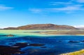 View over black volcanic sand banks on remote  blue and green shimmering water against blue skyand dry hill background Royalty Free Stock Photo