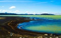 View over black volcanic sand beach on remote blue and green shimmering water against blue sky