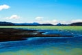 View over black volcanic sand beach on remote blue and green shimmering water against blue sky