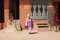 View over dirt square on oriental style house front entrance with one boy sitting on steps and muslim veiled woman with pink tunic