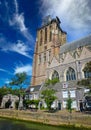 View over dutch water canal on residential houses with medieval gothic church tower background against blue summer sky, fluffy