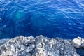 View from over the edge of a rocky cliff to clear blue sea water below Royalty Free Stock Photo