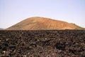 View over field of black volcanic lava rocks on red cone of mountain - Timanfaya NP, Lanzarote