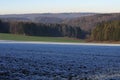 View over frost covered field to hilly forest