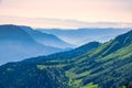 View over the Green Valley, surrounded by high mountains on a pink summer sunset. Layers of mountains in the haze during sunset