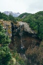 View over Mangawhero Falls rushing down from 20m height of the rocks into a small river. Magnificent peaks of Mt Ruapehu