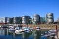 View over marina on modern silver office buildings five boats against blue sky