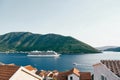 View over the red roofs of houses to a white cruise ship sailing on the sea along the mountains Royalty Free Stock Photo