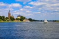 View over river maas on old villaga with church tower, motor boat against blue summer sky - Kessel, Netherlands