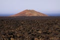 View over rough volcanic lava rocks on red cone of volcano with blurred atlantic ocean background - Timanfaya NP, Lanzarote