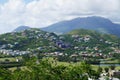 A view over St. Kitts Island with residential area and road on the foreground and lush green hills on the background.