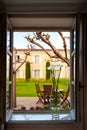 View out of opened window with vase on sill to backyard with patio, formal garden of Chateau Cordeillan-Bages, Bordeaux, France.