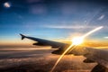 View on passenger aircraft left wing. Sunset shines as a golden light arch over the wing. Thick clouds below airplane are