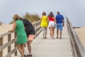 View of pedestrian path on beach, backs of couple with daughter walking on wooden path and other couple talking