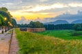 View of pedestrian walking path street with lamps lights on defensive city wall, grass green field, trees and Tuscany hills