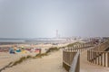 View of pedestrian wooden path on beach, people walking and people taking sunbath on beach, lighthouse as background