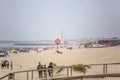 View of pedestrian wooden path on beach, people walking and people taking sunbath on beach, lighthouse as background