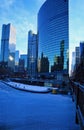 View of pedestrians on a riverwalk on a blue and frigid winter morning in Chicago alongside a frozen river and elevated bridge. Royalty Free Stock Photo