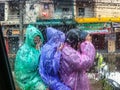 View of people in raincoats on a scooter through a car window with raindrops in Thailand.