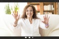 View of a personal computer screen with a portrait of a smiling woman waving during a video call. She is at home