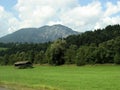 A view of a picturesque meadow on which an old barn is built, behind which picturesque mountains can be seen. Above them is a blue Royalty Free Stock Photo