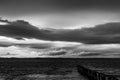 View of a pier on a lake at dusk, beneath a dramatic, moody sky