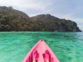View from a pink kayak to the nose of a kayak and a green island in the clear water of the ocean