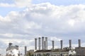 View of the pipes of the plant from which there is white smoke against the sky