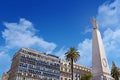 View of The Piramide de Mayo in Buenos Aires, Argentina, surrounded by old buildings and green palm trees, against a